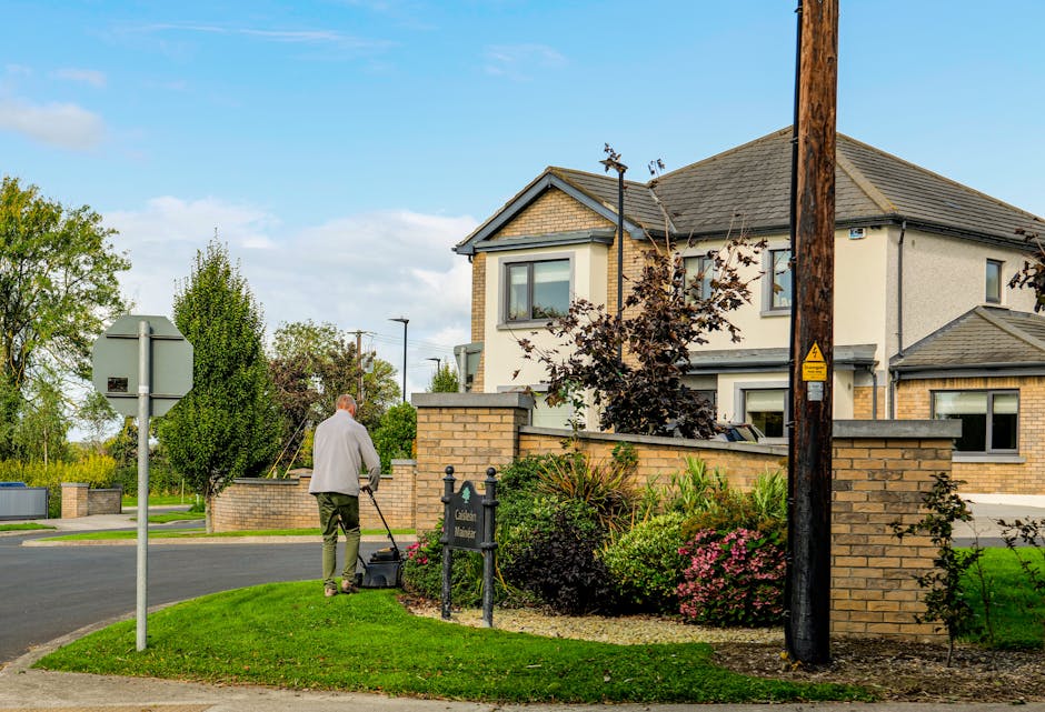 An outdoor garden scene showcasing a neatly maintained lawn with trimmed grass bordered by garden beds filled with a variety of plants. In the background, there are well-shaped hedges and a few small 